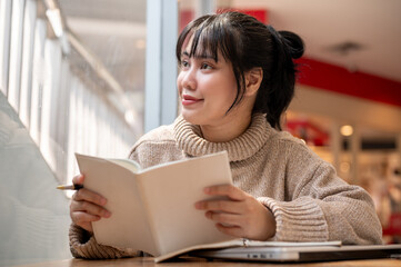Obraz premium A woman is looking out the window and daydreaming while reading a book in a coffee shop.