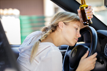 female driver slouched over steering wheel holding beer bottle