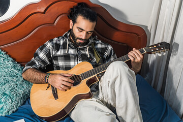 Colombian man playing and studying guitar in his room. Acoustic and harmonic instrument