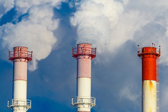 Chimneys with thick smoke of a thermal station against the background of a blue sky. The concept of rendering communal services for heat supply.