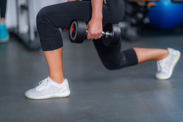Athletic woman performing lunges using weights for strength and endurance training in the gym