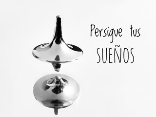 Spanish text Persigue tus sueños and a silver spinning top. A concept for a follow your dreams...