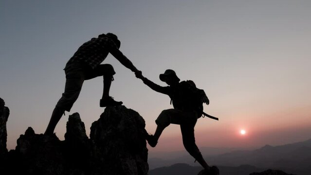 silhouette of People helping each other hike up a mountain at sunrise. Giving a helping hand, and active fit lifestyle concept. help and success concept,  Leadership Concept, teamwork.