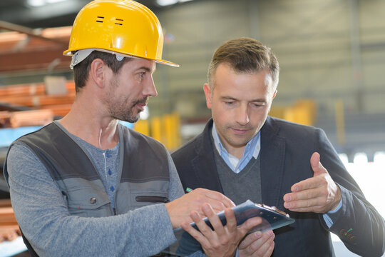 workman in disucssion with suited man looking at clipboard