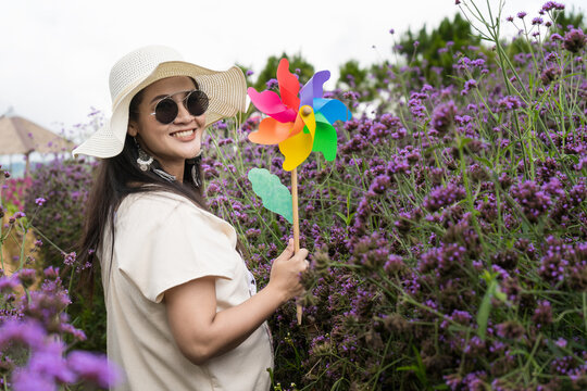  Beautiful woman taking a picture with flowers and holding a brightly colored turbine in garden in the winter of Thailand.