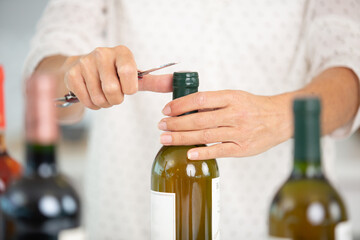 cropped view of hands removing plastic from wine bottle