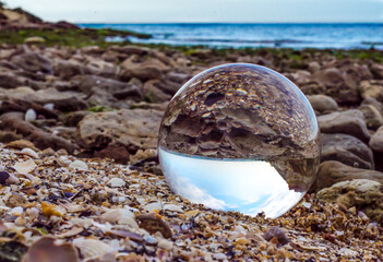 Fototapeta na wymiar glass ball lens lies on the sand of the sea shore landscape