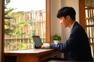 Handsome young businessman drinking hot coffee and reading email on digital tablet at cafe