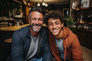 Fototapeta premium Happy mature man is seated next to another young man who is smiling in a bar setting