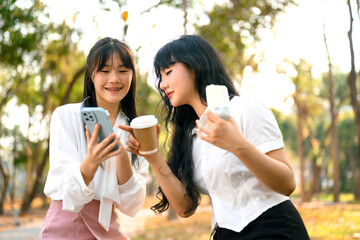 Two attractive young female talking and using mobile phone during lunch break in the park