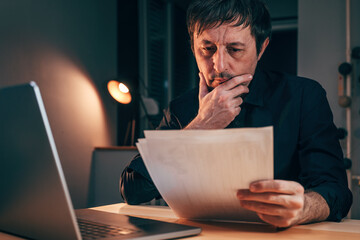 Businessman reading paper document report in business office, exhausted adult male working overtime