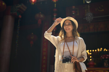 Gorgeous female tourist with camera standing against a Chinese Temple located in Chang Mai Thailand