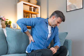 Handsome man touching his back, suffering from backpain, sciatica, sedentary lifestyle concept. Spine health problems. Healthcare, insurance - obrazy, fototapety, plakaty