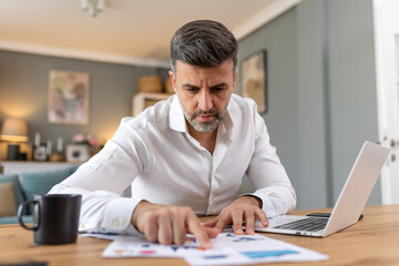 Fototapeta premium Handsome man freelancer noting information for planning project doing remote job via laptop computer. Man reading email on modern laptop device .