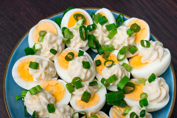 Talerz pełny jajek ugotowanych na twardo przekrojnych na pół, udekorowane majonezem i zielonym szczypiorkiem