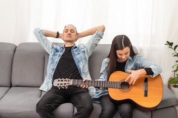 Father guy teaching girl teenager daughter guitar playing at home. Family musical lessons with strings instrument