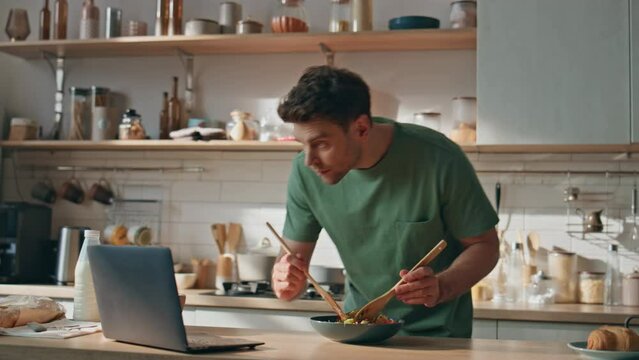 Young man watching video cooking in big kitchen closeup. Hipster looking laptop