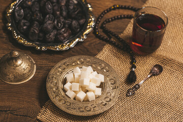 Fototapeta na wymiar Glass of tea with sugar and dried dates on a wooden background with burlap. Ramadan Kareem holiday background. Halal meal set for fasting is obligatory for Muslim on wooden. . Soft focus. Shallow DOF.
