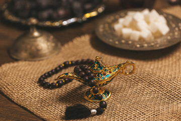 Arabian vintage lamp with wooden rosary beads on wooden background with burlap dates and sugar. Ramadan Kareem holiday background. Islamic Holy Month Greeting Card. Soft focus. Shallow DOF.