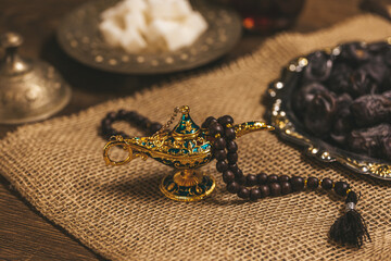 Arabian vintage lamp with wooden rosary beads on wooden background with burlap dates and sugar. Ramadan Kareem holiday background. Islamic Holy Month Greeting Card. Soft focus. Shallow DOF.