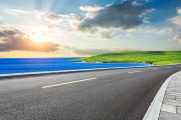 Asphalt highway road and blue lake with green grass nature landscape at sunset