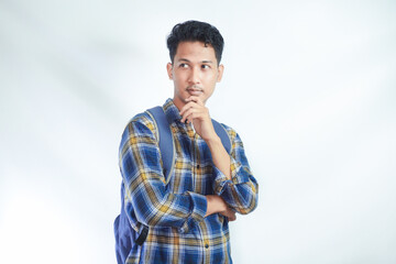 pensive young Asian student man in casual clothes with backpack standing put hand prop up on chin looking aside up isolated on white background. High school university college concept