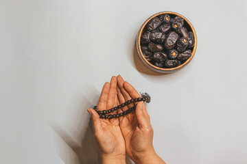 Wooden rosary in a woman's hand and dried dates in a wooden bowl. Ramadan kareem background