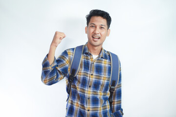Excited young Asian man student wearing flannel shirt with backpack making winner gesture and celebrating success isolated on white background. Education in high school university college concept