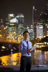 Chinese businessman outdoors at night using his digital tablet device.