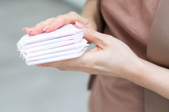 Young adult woman hand holding packs of sanitary towel on light p background. Pastel color. Closeup. Empty place for text.