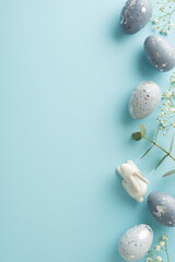 Festive Easter vertical top view arrangement in an image showcasing slate greyish eggs, a miniature bunny, gypsophila, and eucalyptus on a light blue backdrop, with space for text