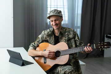 Obraz premium Young soldier playing guitar at home