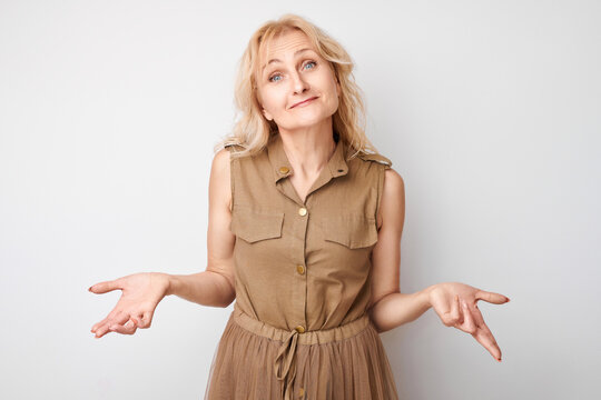 Confused middle-aged woman shrugging her shoulders in uncertainty, isolated on a white background.