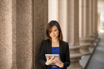 Asian businesswoman outside Colonial building using tablet.