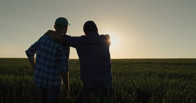 A man and his son watch the sunrise over a wheat field together. Farmers in the field and family business