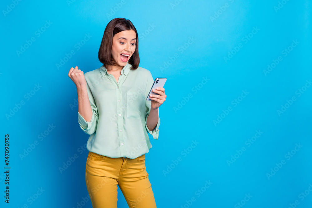 Wall mural Photo of ecstatic woman with bob hairstyle dressed teal shirt look at smartphone scream yeah win bet isolated on blue color background