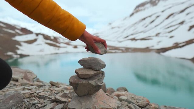 Hand of girl builds a balancing stone pile in the crystal-clear water at Blue lake named Suraj Tal in Lahaul, Himachal Pradesh, India. Nature and landscape themes. Pile Of Stones at  lake in mountains