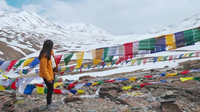 Indian young woman touching prayer flags and walks on mountain at Baralacha La Pass, Himachal Pradesh, India. Tourist exploring mountains and monasteries during travel vacation. 