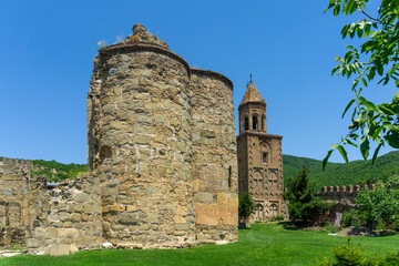 Fototapeta na wymiar Monastery courtyard. Ruins of old church on the green grass. Stone wall of tower. Brick bell tower. Daylight, blue sky.