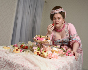 Close up portrait of cute female model wearing an opulent pink gown, the costume of a historical French baroque nobility.  sitting at table with sweet cakes and indulgent food feast.