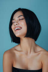 Obraz premium A joyful young woman with short black hair is captured mid-laugh, her eyes gently closed and a broad smile illuminating her face