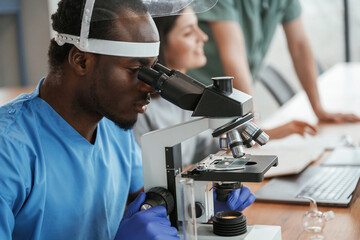 Working in a lab with test tubes and microscope. Group of doctors are together indoors