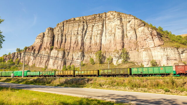 Russia, Chelyabinsk region, July 2021: a freight train arrives by rail under a red rock in the city of Minyar on a summer sunny day.