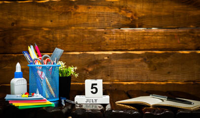 July calendar with number  5. Office background with pencils pens and ruler copy space. Beautiful background planner calendar on a brown wooden background, space for text.