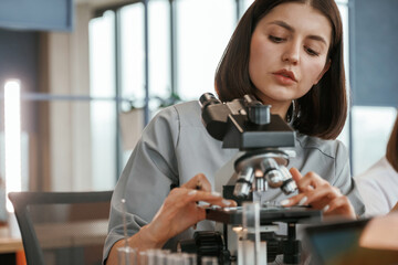By the microscope. Female doctor in coat is indoors