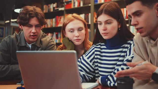 Four young adults deeply involved in group discussion over laptop in library setting, symbolizing collaboration and focused teamwork