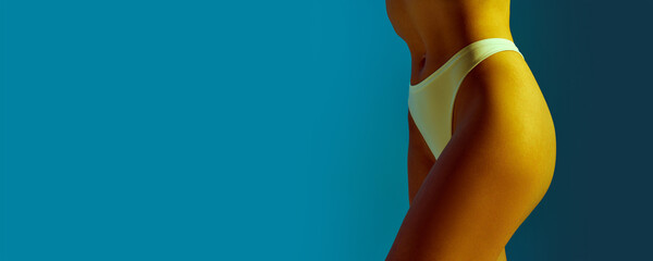 Banner. Cropped portrait of young woman in lingerie posing in yellow neon light against gradient blue background. Concept of beauty treatments, dieting, female health, femininity, spa procedures. - obrazy, fototapety, plakaty