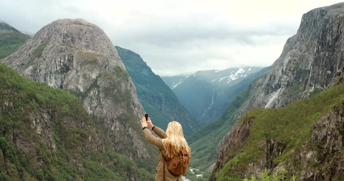 Woman, tourist and phone for video, mountain and norwegian lake view with backpack and sightseeing. Technology, adventure and nature for vacation, hiking and travel in outdoor for photography