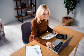 Photo of financial analytic blonde hair mature woman in brown sweater working with paper count market isolated indoors office workplace