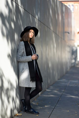 Girl in a hat and coat standing against the wall